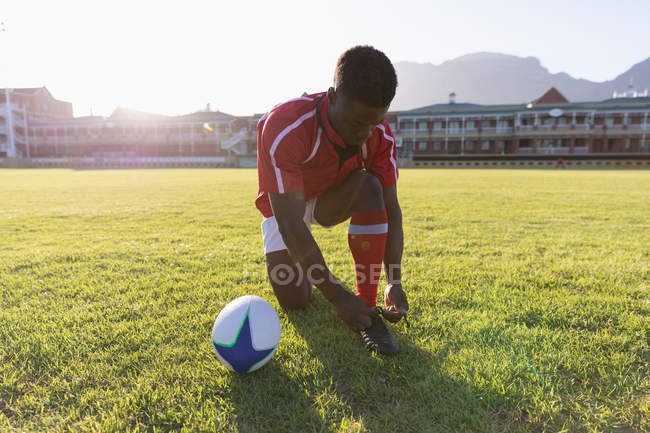 Vue de face d'un joueur de rugby afro-américain masculin attachant ses lacets dans le stade — Photo de stock