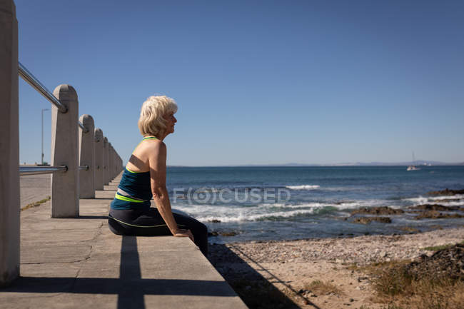 Вид збоку на вдумливу активну старшу жінку, яка відпочиває на кордоні набережної під сонцем — стокове фото