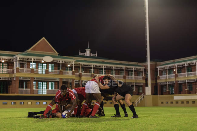 Vista lateral de jugadores de rugby multiétnicos que juegan al rugby en el estadio por la noche - foto de stock