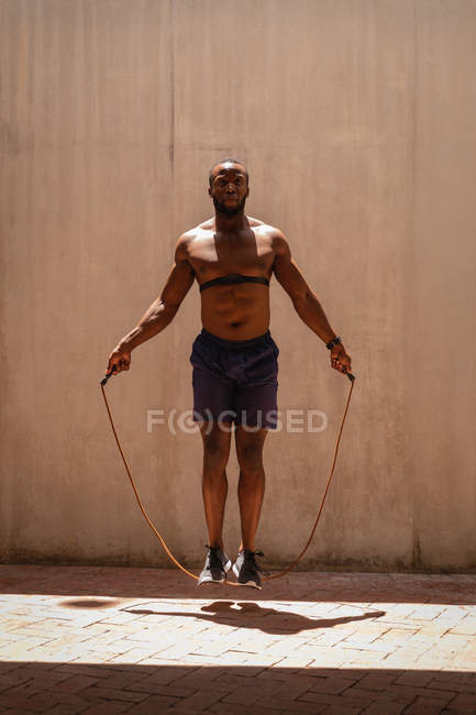 Front view of young African-American fit man doing skipping exercise with rope under the bridge — Stock Photo