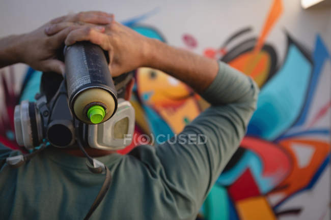 Vista trasera del joven artista de graffiti caucásico sosteniendo spray de pintura en la fuente de la pared - foto de stock