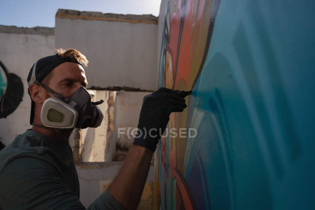 Side view of young Caucasian graffiti artist drawing with marker on weathered wall — Stock Photo