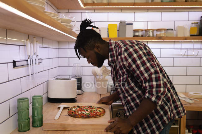 Seitenansicht eines gutaussehenden afrikanisch-amerikanischen Mannes, der zu Hause in der Küche zubereitete Pizza betrachtet — Stockfoto