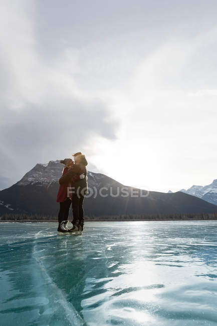 Low angle view of happy Caucasian couple kissing each other in natural snowy landscape with ice skates to their foot — Stock Photo