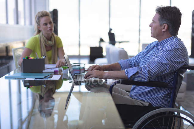 Vista lateral de hombre caucásico maduro discapacitado y mujer rubia caucásica ejecutiva interactuando entre sí en la oficina - foto de stock