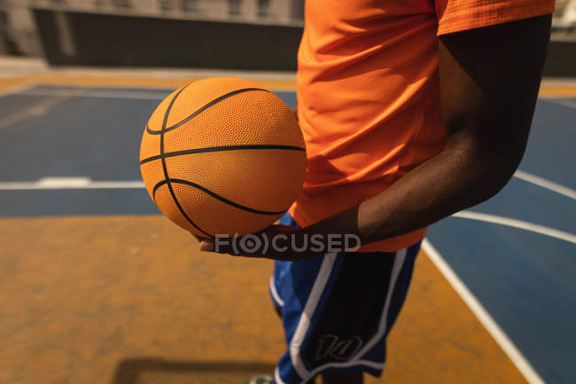 Sección media del jugador de baloncesto de pie con baloncesto en el patio - foto de stock