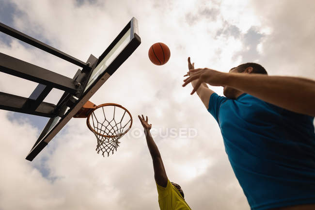 Низький кут зору багатоетнічних гравців, які грають у баскетбол на баскетбольному майданчику — стокове фото