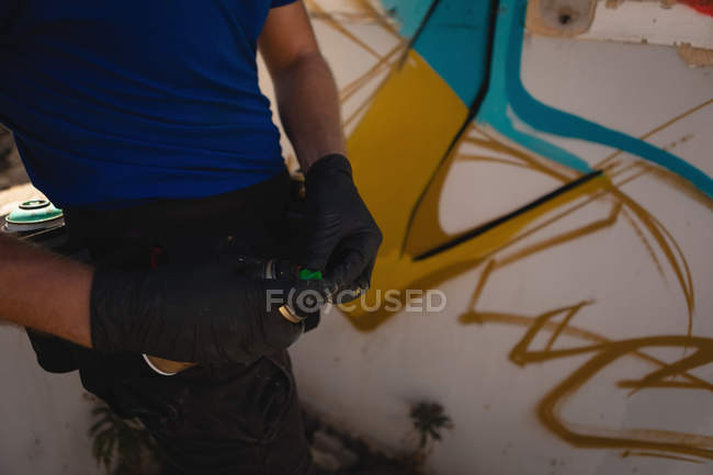 Sección media del artista de graffiti sosteniendo pintura en aerosol mientras está de pie en el callejón - foto de stock