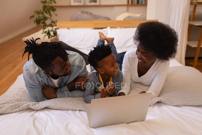 Vista frontale di felice famiglia afro-americana insieme godendo durante l'utilizzo del computer portatile a casa. Stanno sorridendo. — Foto stock
