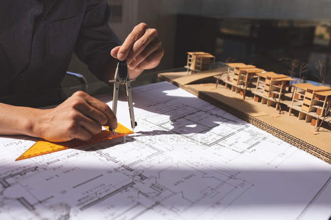 Mittlerer Abschnitt eines männlichen Architekten, der am Entwurf arbeitet und Geometriekompass am Schreibtisch in einem modernen Büro verwendet — Stockfoto