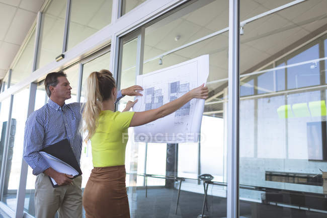 Side view of mature Caucasian male and Caucasian blonde female architects discussing over blueprint in the office — Stock Photo