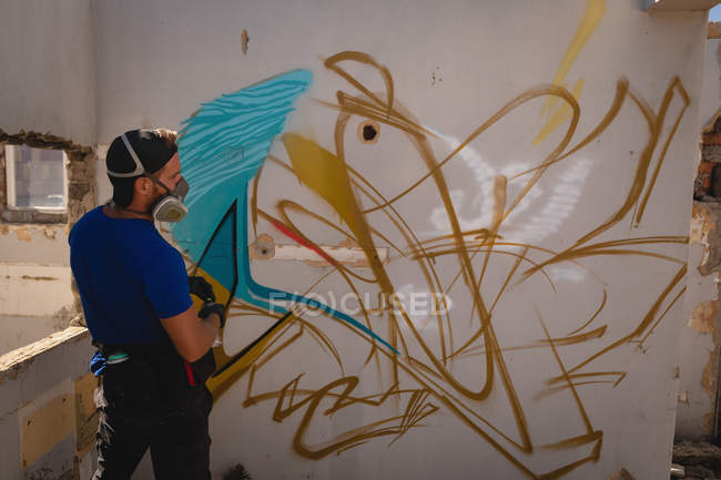 Заднього вигляду вдумливі молодих кавказьких художника графіті дивлячись на вивітрюванню стіни кімнати — стокове фото