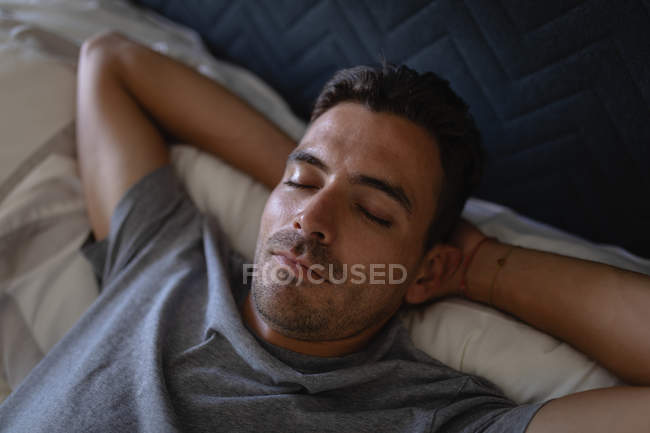 Vista de ángulo alto del joven hombre caucásico relajándose mientras está acostado en la cama en casa - foto de stock