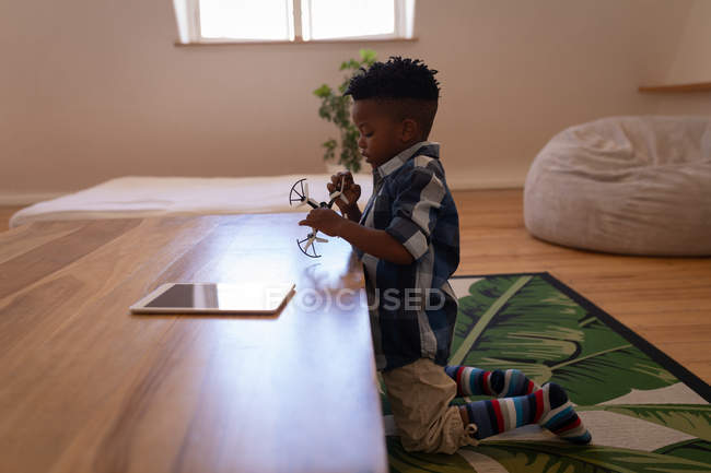 Vista laterale del piccolo ragazzo afro-americano carino che gioca con il drone a casa — Foto stock