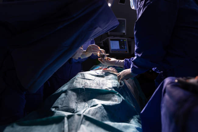 Vista lateral de cirujanos concentrados realizando operación en quirófano en el hospital - foto de stock