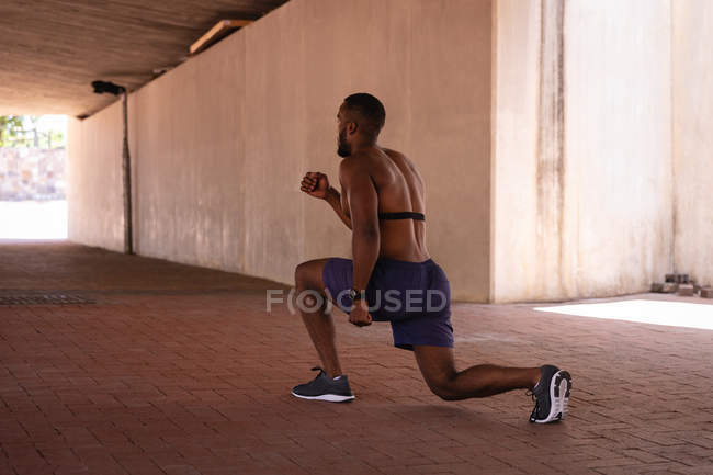 Vista posteriore del giovane afroamericano in forma che fa esercizio di stretching sotto il ponte — Foto stock
