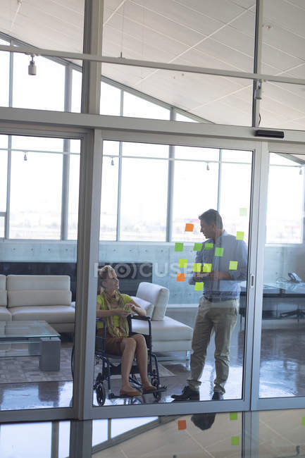 Front view of disabled Caucasian blonde female and Caucasian male executive discussing over sticky notes in the office — Stock Photo