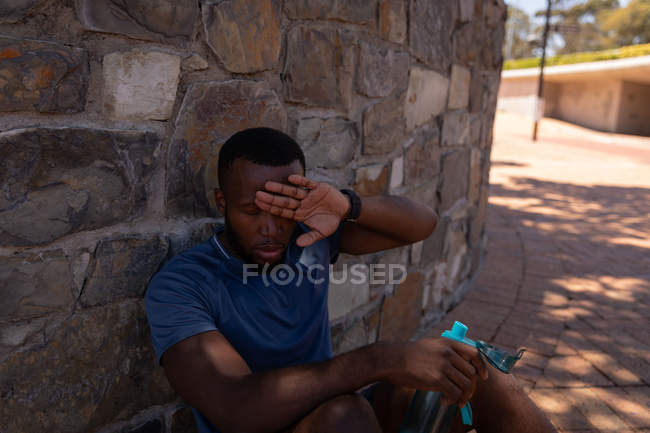 Vue de face du jeune homme en forme afro-américain se relaxant à côté du mur par une journée ensoleillée — Photo de stock