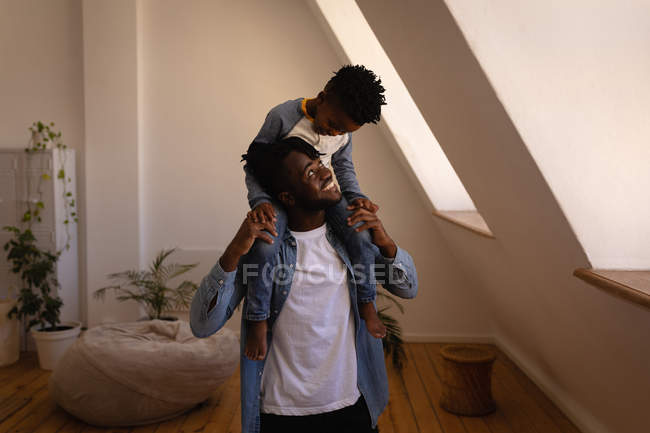 Front view of happy African-American father carrying son on shoulders at home — Stock Photo