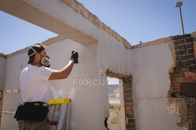 Side view of young Caucasian graffiti artist spray painting weathered wall at alley — Stock Photo