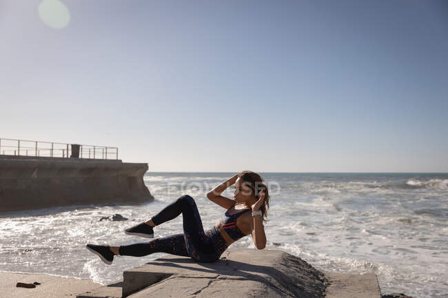 Vue latérale de la femme faisant de l'exercice à la plage par une journée ensoleillée — Photo de stock
