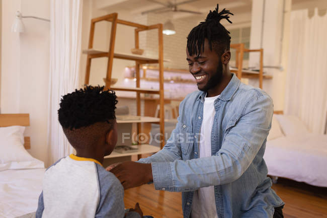 Vue latérale du beau père afro-américain habiller son fils à la maison — Photo de stock