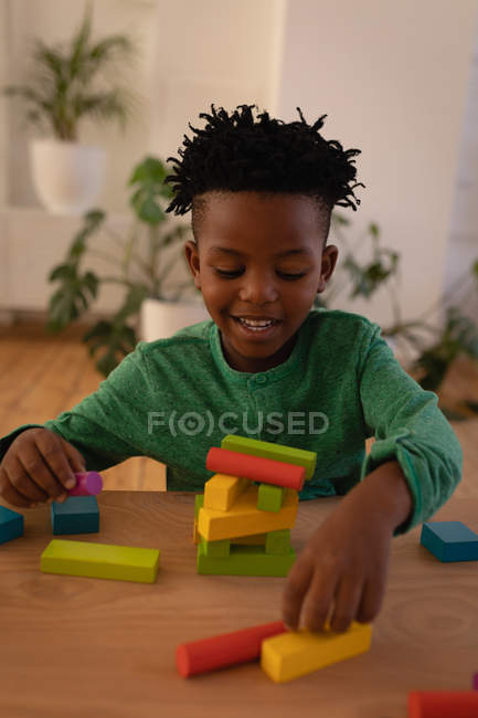Vista frontal de un niño afroamericano lindo jugando con bloques de construcción en casa. Él sonríe. - foto de stock