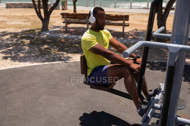 Vista lateral de un joven afroamericano en forma haciendo ejercicio de espalda máquina de remo en un día soleado - foto de stock