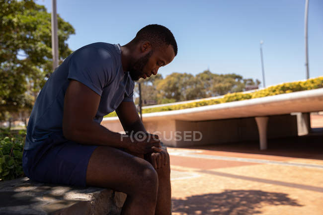 Вид збоку молодих афро-американських fit чоловік дивиться на смарт-дивитися відпочиваючи на стороні вулиці — стокове фото