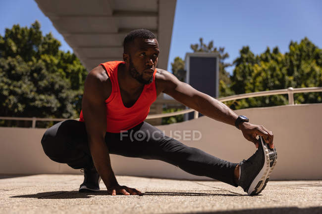 Vista frontal do jovem afro-americano em forma de homem fazendo exercício sob a ponte em um dia ensolarado — Fotografia de Stock