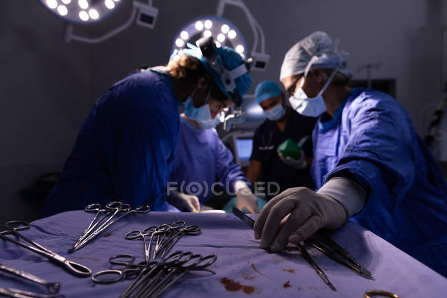 Низкий угол обзора хирургов, сконцентрированных на выполнении операции в операционной в больнице с ножницами на переднем плане — стоковое фото