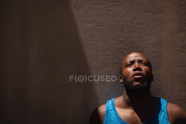 Vista frontal do pensativo jovem afro-americano em forma homem de pé ao lado da parede em um dia ensolarado — Fotografia de Stock