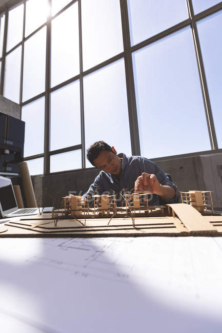 Вигляд спереду чоловічого азіатських архітектора працює над офісної будівлі модель зі своєю ноутбука та інструменти у сучасні офісні — стокове фото