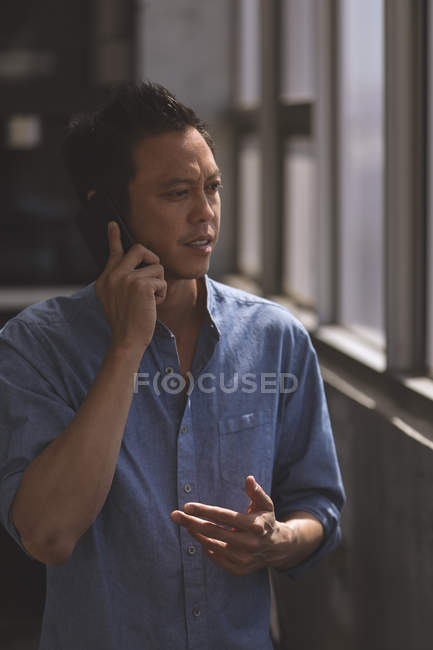 Вид спереди молодого азиатского мужчины-руководителя, разговаривающего по мобильному телефону в офисе — стоковое фото