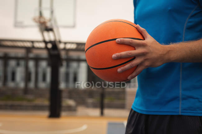 Середня секція баскетболіста, що стоїть з баскетболом на ігровому майданчику — стокове фото