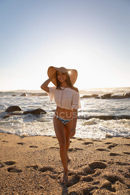 Vorderansicht einer glücklichen Frau, die an einem sonnigen Tag am Strand spazieren geht. sie lächelt — Stockfoto