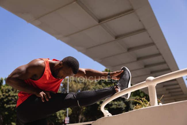 Vista laterale del giovane afro-americano in forma che fa esercizio sotto il ponte sulla ringhiera — Foto stock