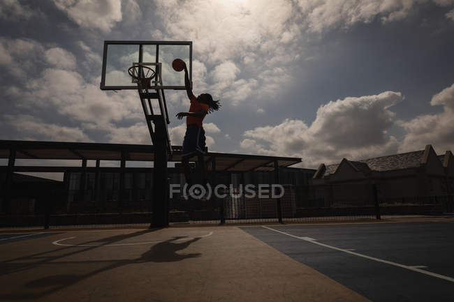 Low angle view of African-American basketball player playing basketball at basketball court in back lit — Stock Photo