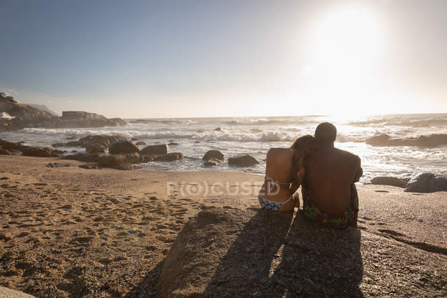 Visão traseira do jovem casal multi-étnico relaxante na praia — Fotografia de Stock