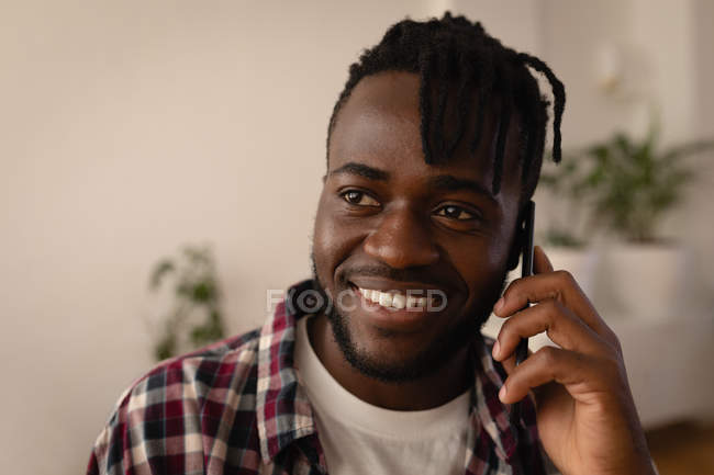 Um belo afro-americano a falar ao telemóvel em casa. Ele está sorrindo. — Fotografia de Stock