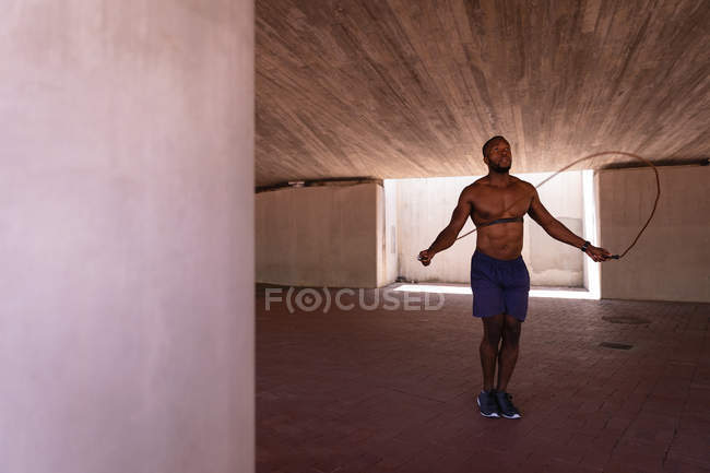 Frontansicht eines jungen afrikanisch-amerikanischen fitten Mannes, der mit dem Seil unter der Brücke springt — Stockfoto