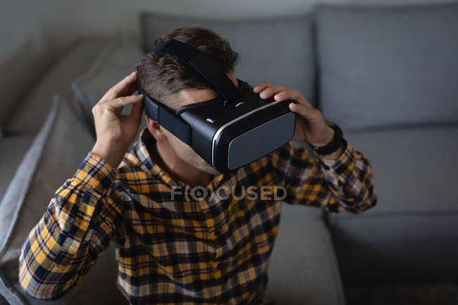 Vista ad alto angolo di giovane uomo caucasico utilizzando cuffia realtà virtuale seduto sul divano a casa — Foto stock