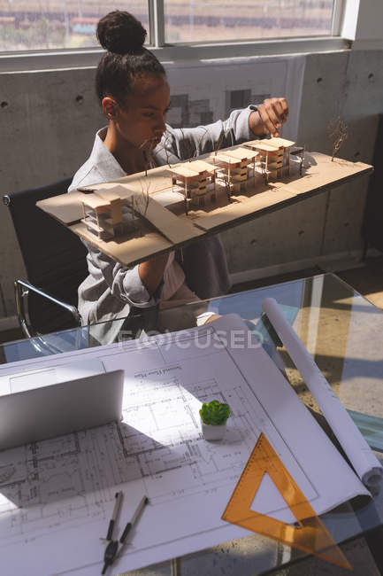 Front view of young mixed race businesswoman looking at office model in the office — Stock Photo