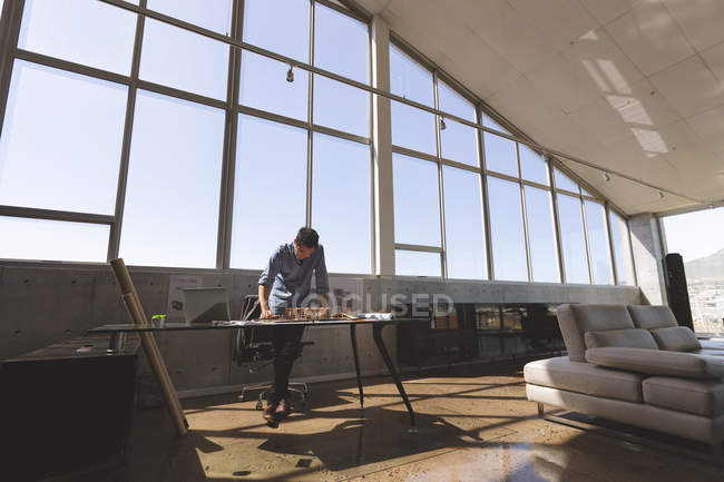 Vista frontal del arquitecto asiático trabajando en el modelo arquitectónico en el escritorio en una oficina moderna - foto de stock