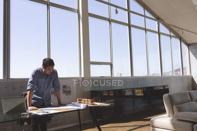 Вигляд спереду азіатських чоловічого архітектора стоячи реєстрації і дивлячись blueprint в сучасні офісні — стокове фото