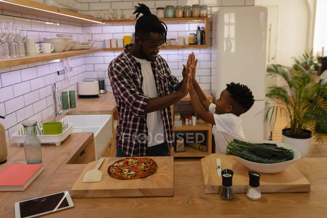Vue latérale du père afro-américain heureux donnant cinq à son fils tout en finissant la cuisine — Photo de stock