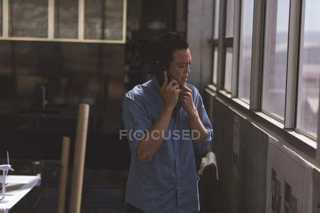 Вид азиатского архитектора-мужчины, разговаривающего по мобильному телефону в современном офисе — стоковое фото