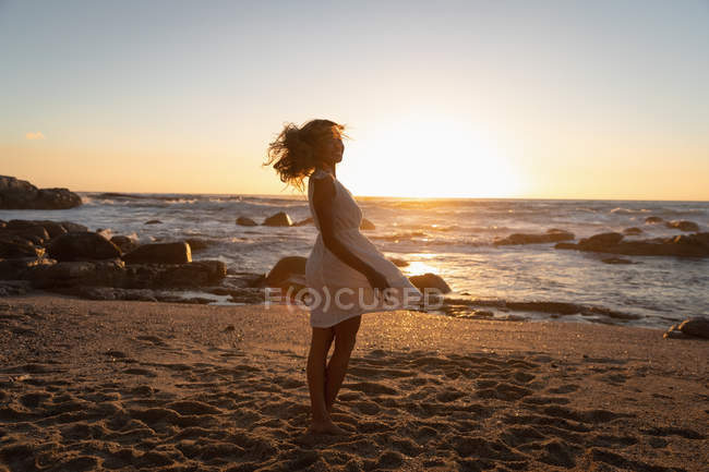 Vista lateral de la mujer disfrutando y bailando en la playa al atardecer - foto de stock