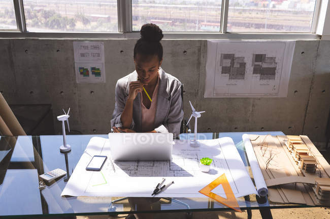 Vista frontal da mulher de negócios de raça mista usando laptop na mesa no escritório de arquitetura — Fotografia de Stock