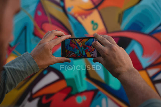 Vista trasera de un joven artista de graffiti caucásico que captura una foto de una pared pintada - foto de stock